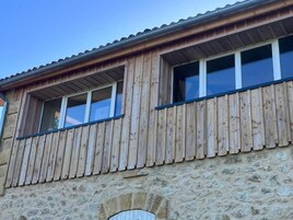 Un edificio con revestimiento de madera y paredes de piedra, que cuenta con dos ventanas con marcos blancos y un pequeño balcón.