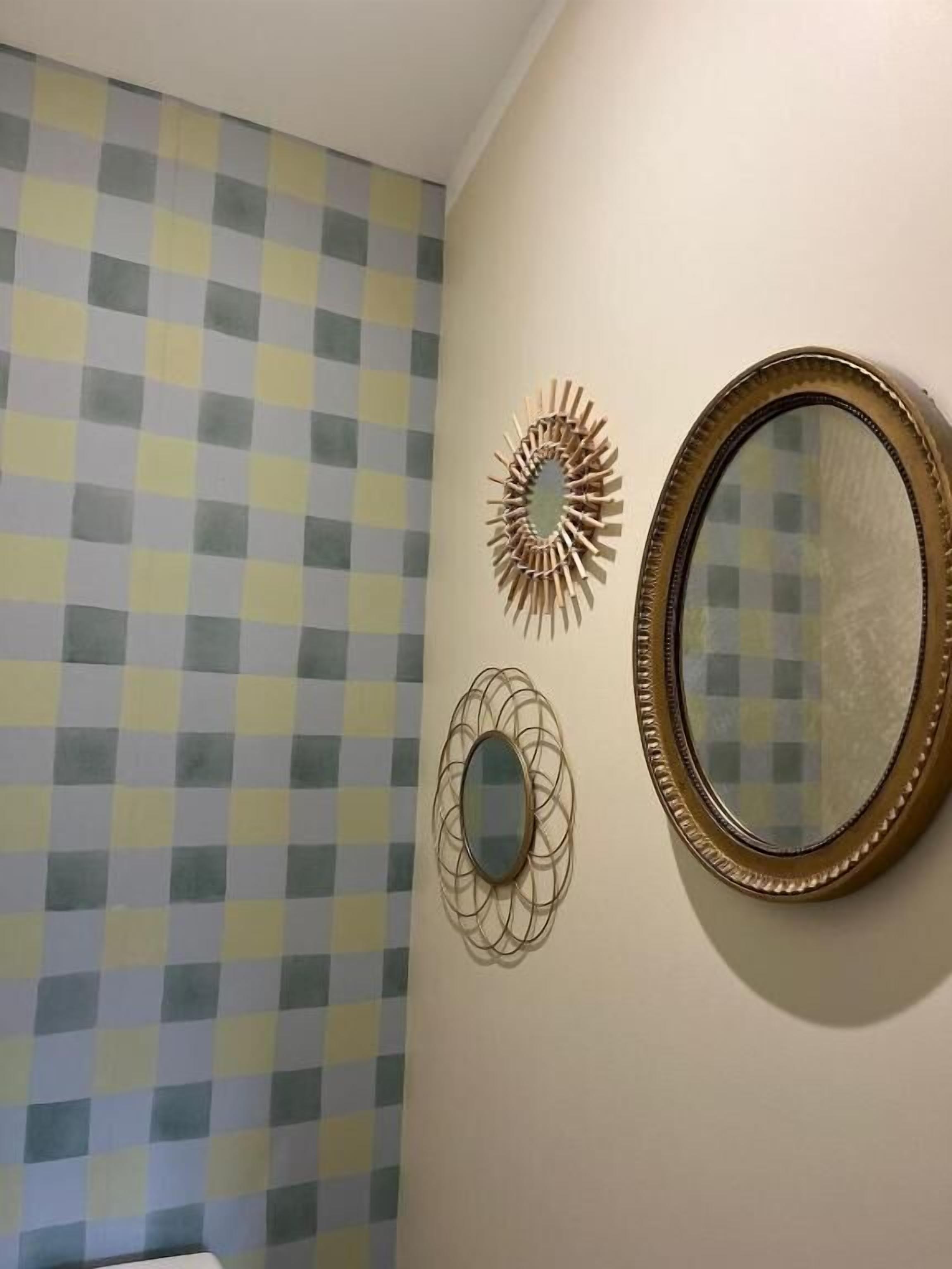 A bathroom with a checkered wall pattern, a round mirror, and two wall-mounted decorative items.