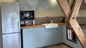 Une cuisine avec des meubles gris, un réfrigérateur en acier inoxydable, un four à micro-ondes et une structure de plafond en bois.