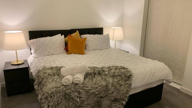 A neatly made bed with a fluffy rug, two bedside lamps, and a dark headboard. - House- Sleeps 6 & Free Parking (Grays)