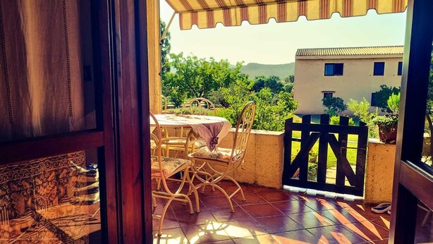 Une terrasse avec une table et des chaises, une vue sur la verdure et les bâtiments, et un portail en bois.