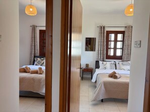 A bedroom with two beds, a window, and a nightstand. - St Visianos Stone House (Filousa)