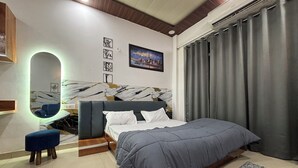 A modern bedroom with a bed, a mirror, a small stool, and a painting on the wall. - Sunshine Stays, Gaur City Centre, Gr Noida West (Greater Noida)