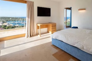 A bedroom with a bed, a desk, a TV, and a view of a coastal area. - ELITE COLLECTION- VILLA GODDESS (Porto Cervo)