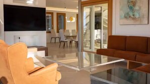 Un soggiorno moderno con un tavolino in vetro, divani in pelle, una TV a schermo piatto e una scala che conduce a un piano superiore.