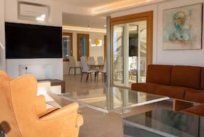 A modern living room with a glass coffee table, leather sofas, a flat-screen TV, and a staircase leading to an upper floor. - ELITE COLLECTION- VILLA GODDESS (Porto Cervo)