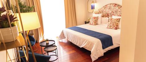 A hotel room with a bed, bedside table, lamp, chair, and potted plant.