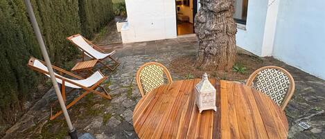 An outdoor patio with a round wooden table, four patterned chairs, and a tree.