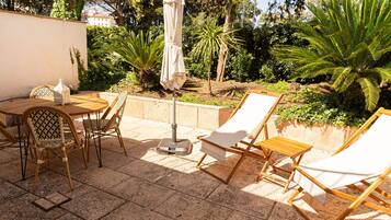 An outdoor patio with a table, chairs, a sun umbrella, and lounge chairs.