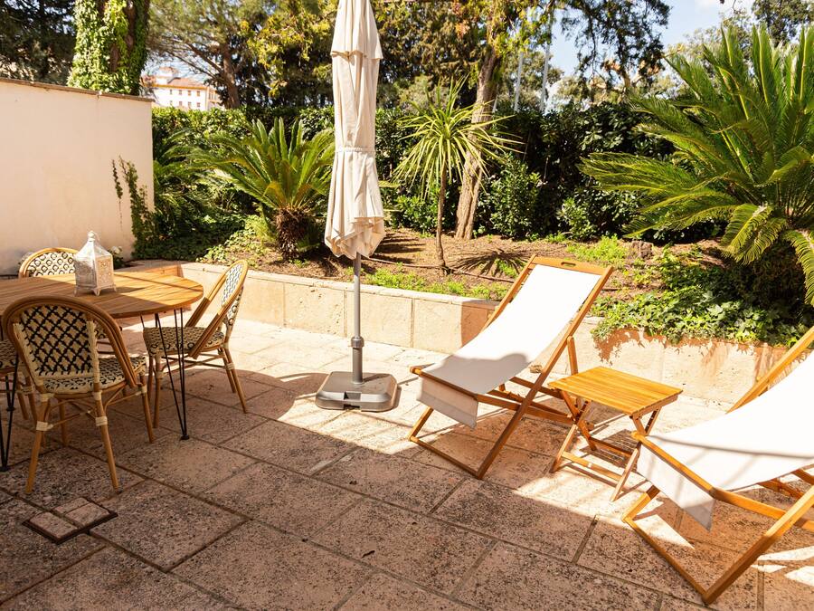 An outdoor patio with a table, chairs, a sun umbrella, and lounge chairs.