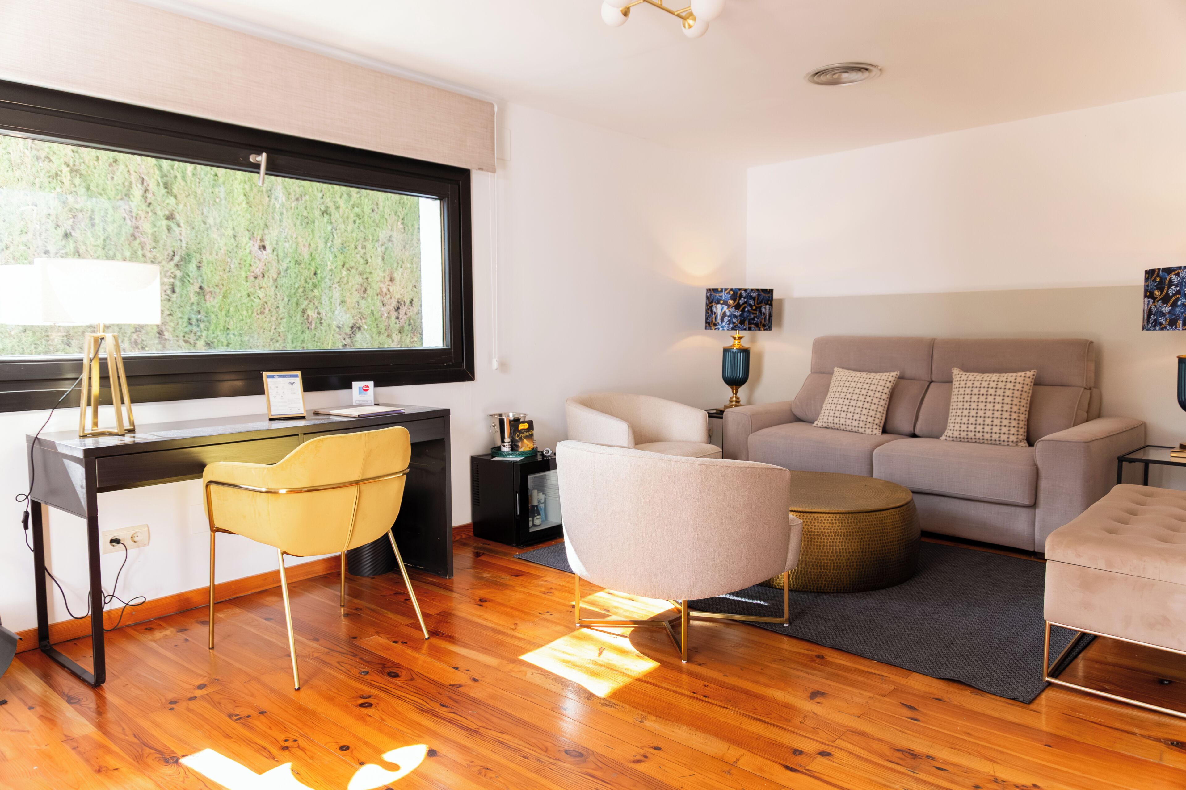 Un salon moderne avec un plancher en bois, un bureau, une chaise jaune, un canapé gris et un pouf rond.