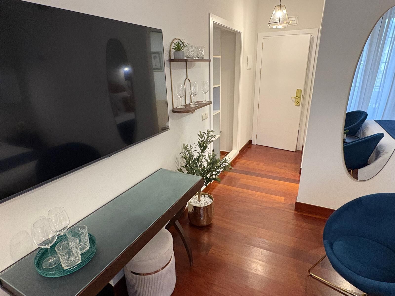 Ein modernes Wohnzimmer mit Flachbildfernseher, einer Essecke mit Tisch und Stühlen, einem Blumentopf und einem Flur, der in einen anderen Raum führt.