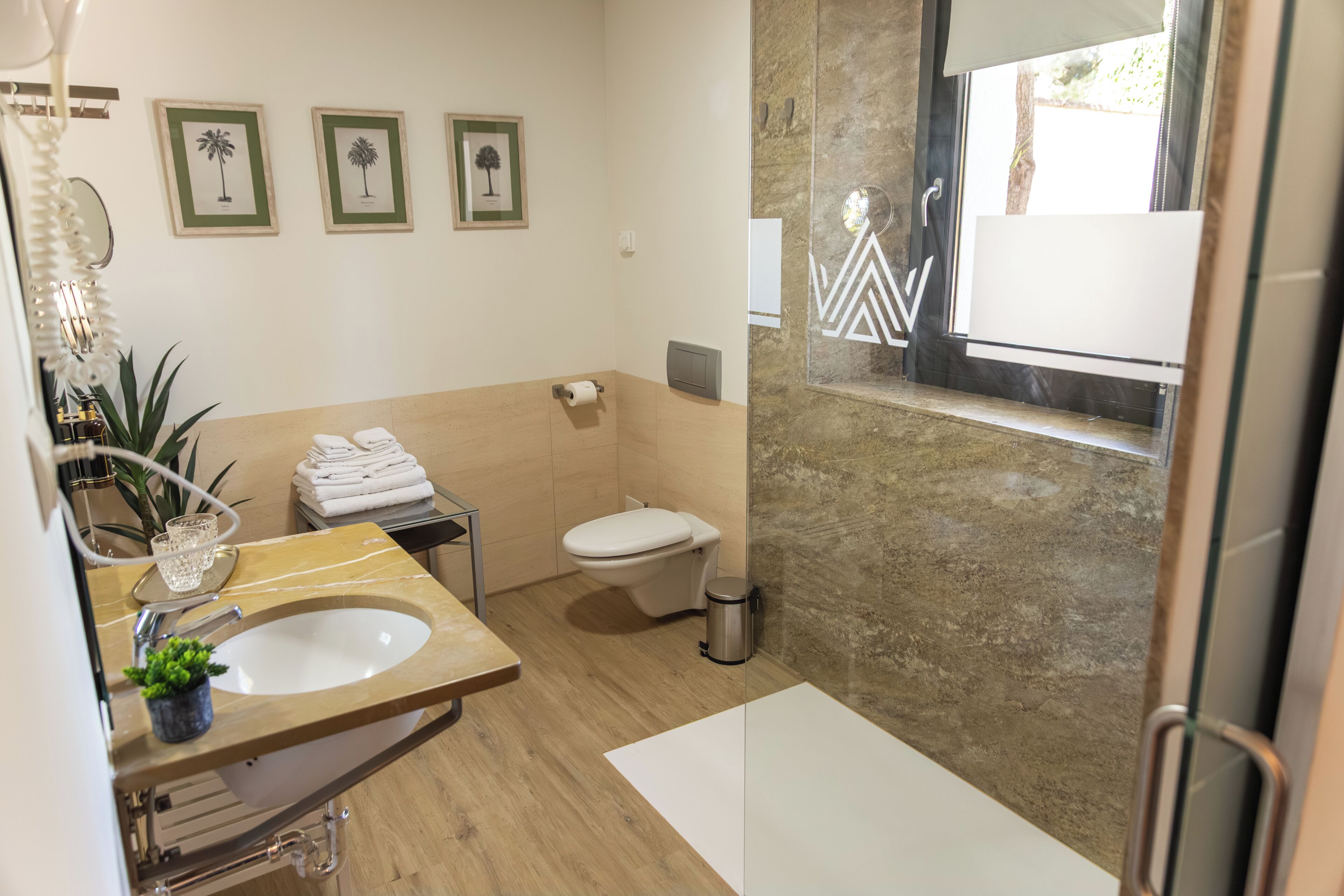 A modern bathroom with a marble sink, toilet, and a small window with a view.