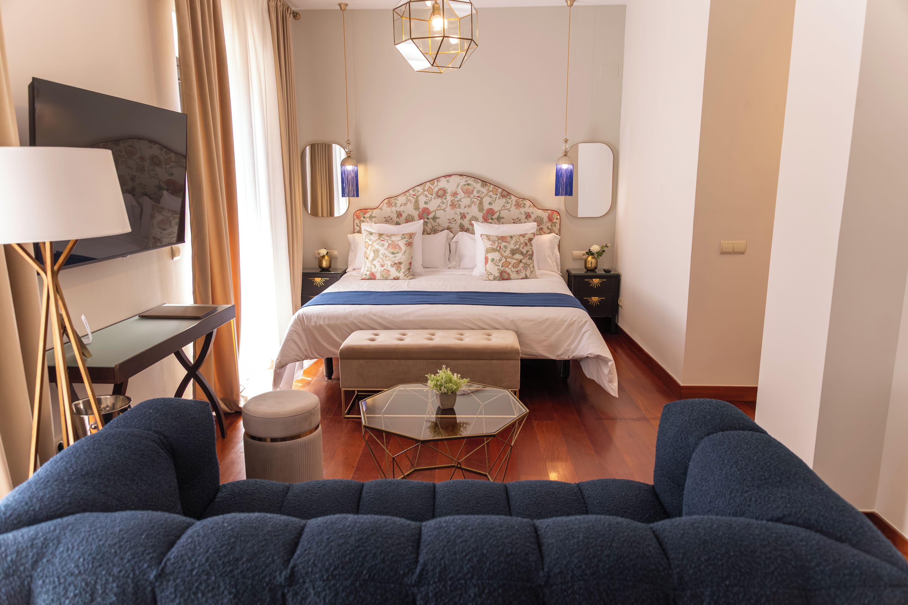 A bedroom with a bed, bedside tables, a desk, a chair, a sofa, and a small table with a plant.