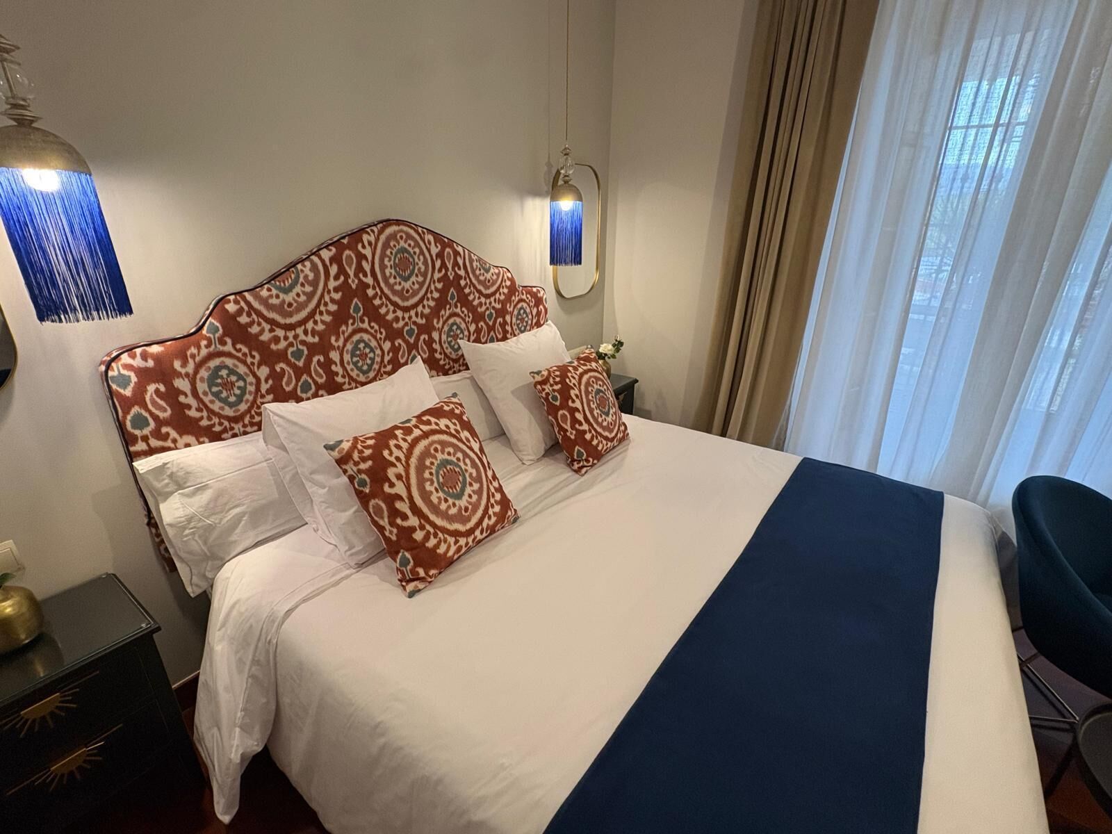 A hotel room with a large bed, a nightstand, a lamp, and a chair.