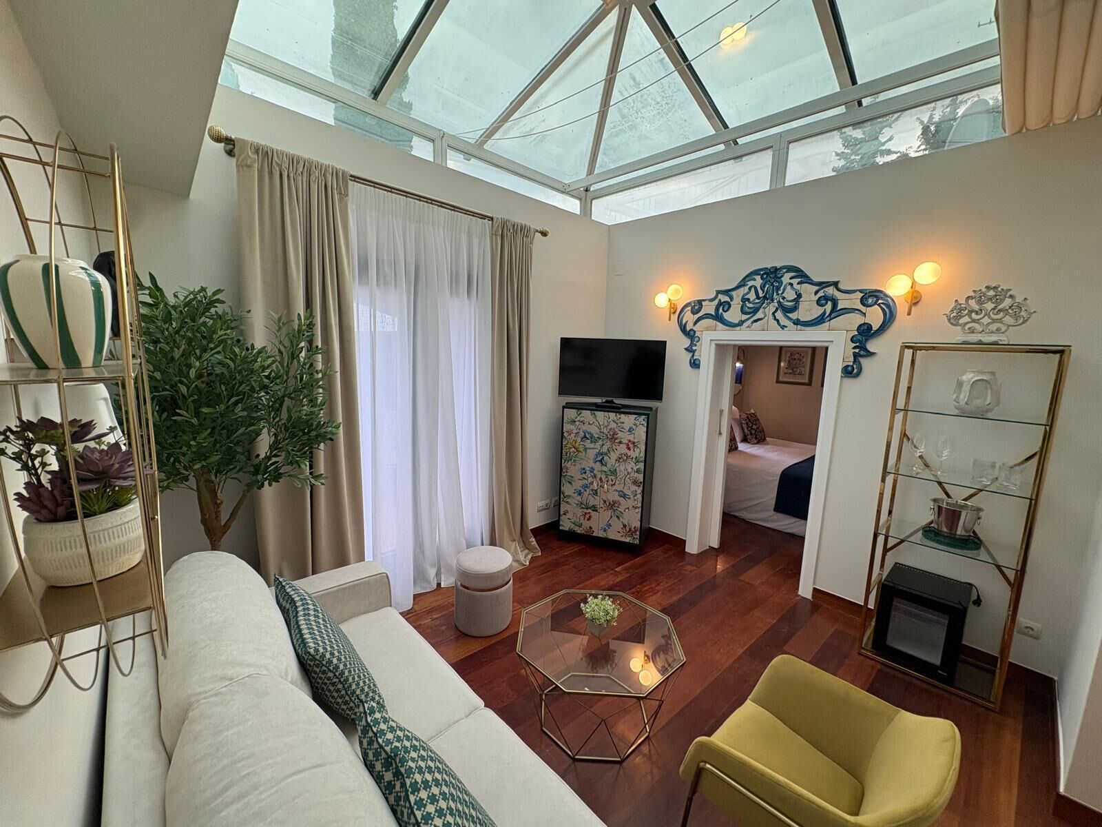 A modern living room with a glass ceiling, a sofa, a yellow armchair, a TV, and a small table.