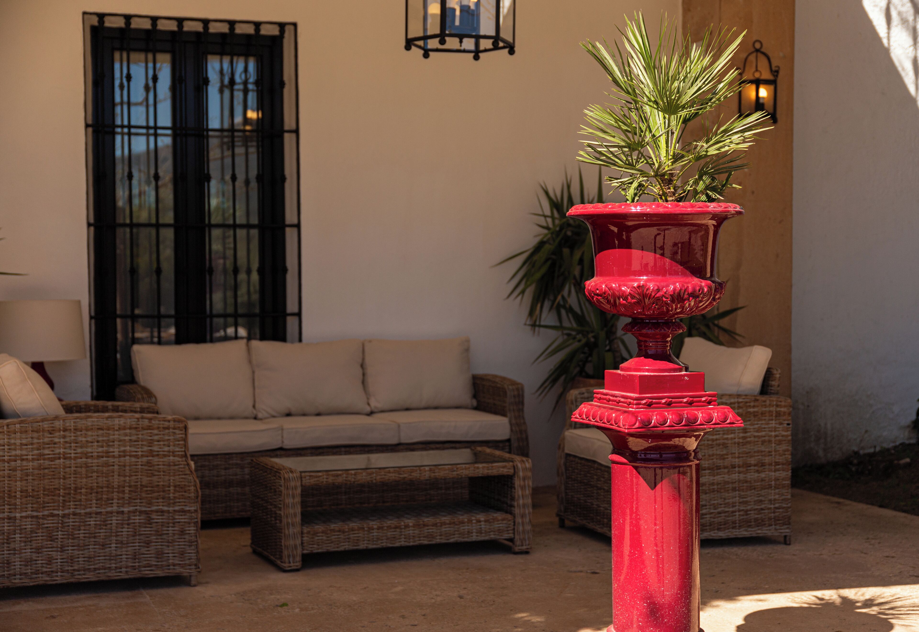 A wicker sofa, a red decorative planter, and a black-framed window.