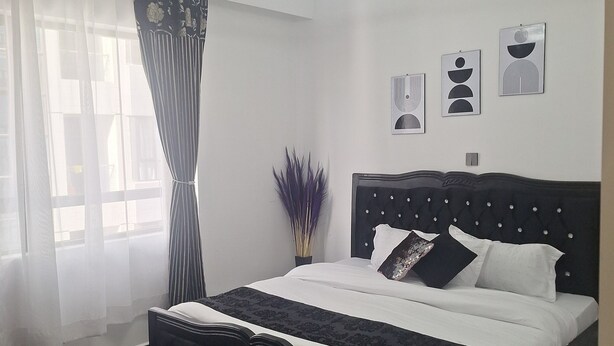 Un dormitorio con cama, ventana con cortinas, lámpara de pared y pared decorada con cuadros.