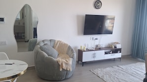 Una sala de estar moderna con un sillón informal redondo, un televisor de pantalla plana montado en la pared, un mueble blanco y un comedor con una mesa y sillas blancas.