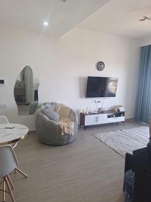 Ein modernes Wohnzimmer mit einem runden Sitzsack, einem flachbildfernseher an der Wand, einem weißen Schrank und einem Essbereich mit weißem Tisch und Stühlen.