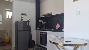 Cocina moderna con armarios blancos, encimera negra y refrigerador de acero inoxidable. Hay un comedor con mesa y sillas blancas.