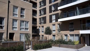 Un edificio residencial de varios pisos con balcones, un patio empedrado y un pequeño árbol.