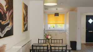 A dining area with a table and chairs, a pendant light, and artwork on the walls. - Runcorn Retreat - 3 Bedroom Cozy House (Warrington)