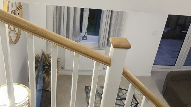 A staircase with white railings and a wooden handrail, leading to a room with a window, a plant, and a lamp. - Runcorn Retreat - 3 Bedroom Cozy House (Warrington)