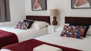 A hotel room with two beds, a nightstand, a lamp, and two framed floral paintings on the walls. - Runcorn Retreat - 3 Bedroom Cozy House (Warrington)