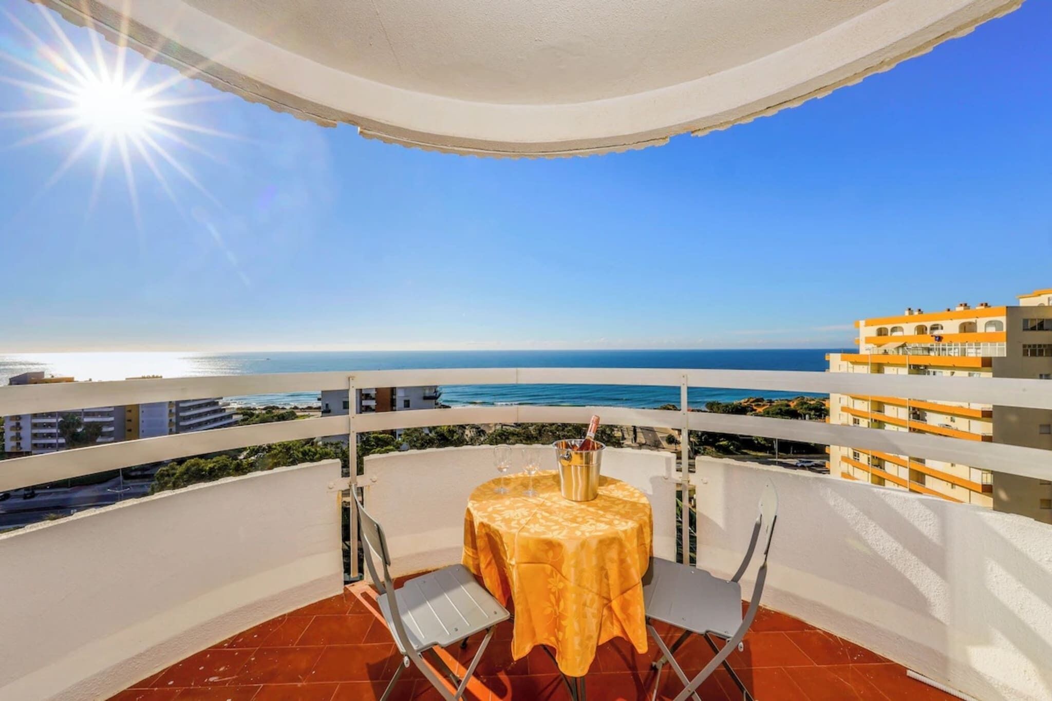 A balcony with a table set for two, overlooking a coastal view.