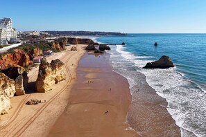 Una playa costera con acantilados rocosos, una orilla de arena y un mar azul transparente.