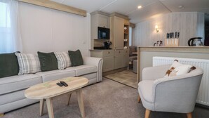 A compact living space with a sofa, a small table, a chair, a kitchenette, and a television. - Lodge 22, Moselle (Malton)