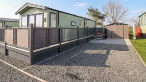 A mobile home with a fenced patio area, a small shed, and a gravel driveway. - Lodge 22, Moselle (Malton)