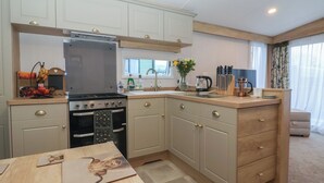A compact kitchen with a stove, oven, and sink, wooden cabinets, and a dining table. - Lodge 22, Moselle (Malton)