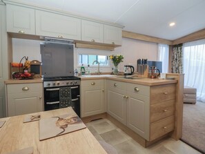 A compact kitchen with a stove, oven, and sink, wooden cabinets, and a dining table. - Lodge 22, Moselle (Malton)