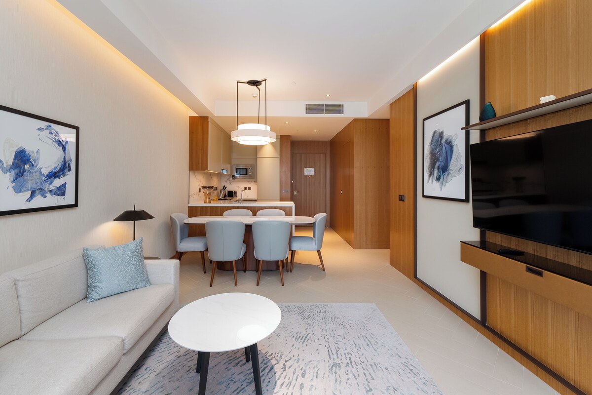 A modern living room with a sofa, a dining table with chairs, a flat-screen TV, and artwork on the walls.
