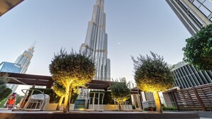 Un rascacielos alto con un diseño distintivo que se estrecha hacia arriba, rodeado de árboles y edificios modernos.