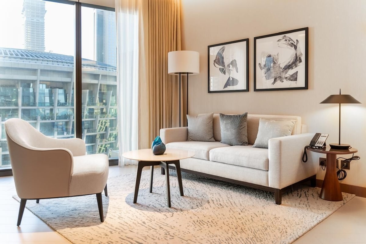 A modern living room with a sofa, armchair, coffee table, and artwork on the wall.
