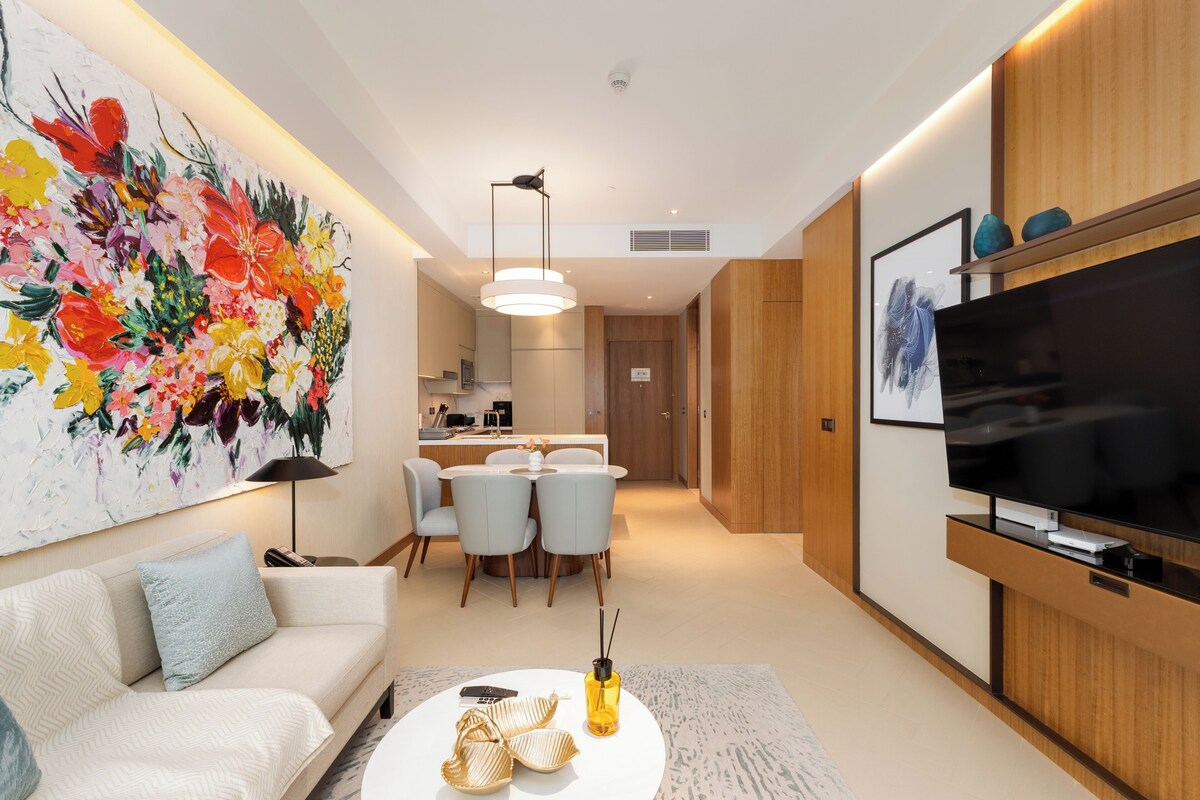 A modern living room with a sofa, a dining area, a TV, and a large floral painting.