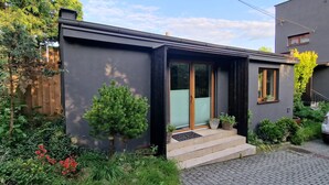 A modern house with a dark exterior, a front door with a glass panel, a small porch, and steps leading to the entrance. - Jakby Poza Miastem (Kraków)