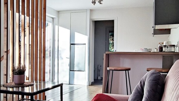 A modern living room with a sofa, a coffee table, and a kitchen area in the background. - Jakby Poza Miastem (Kraków)