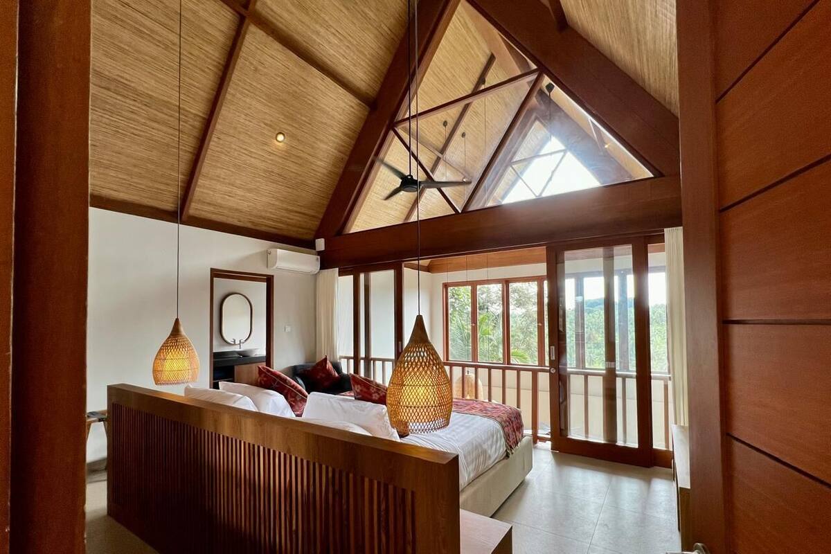 Un dormitorio con techo de madera, ventanas amplias y una cama con almohadas.