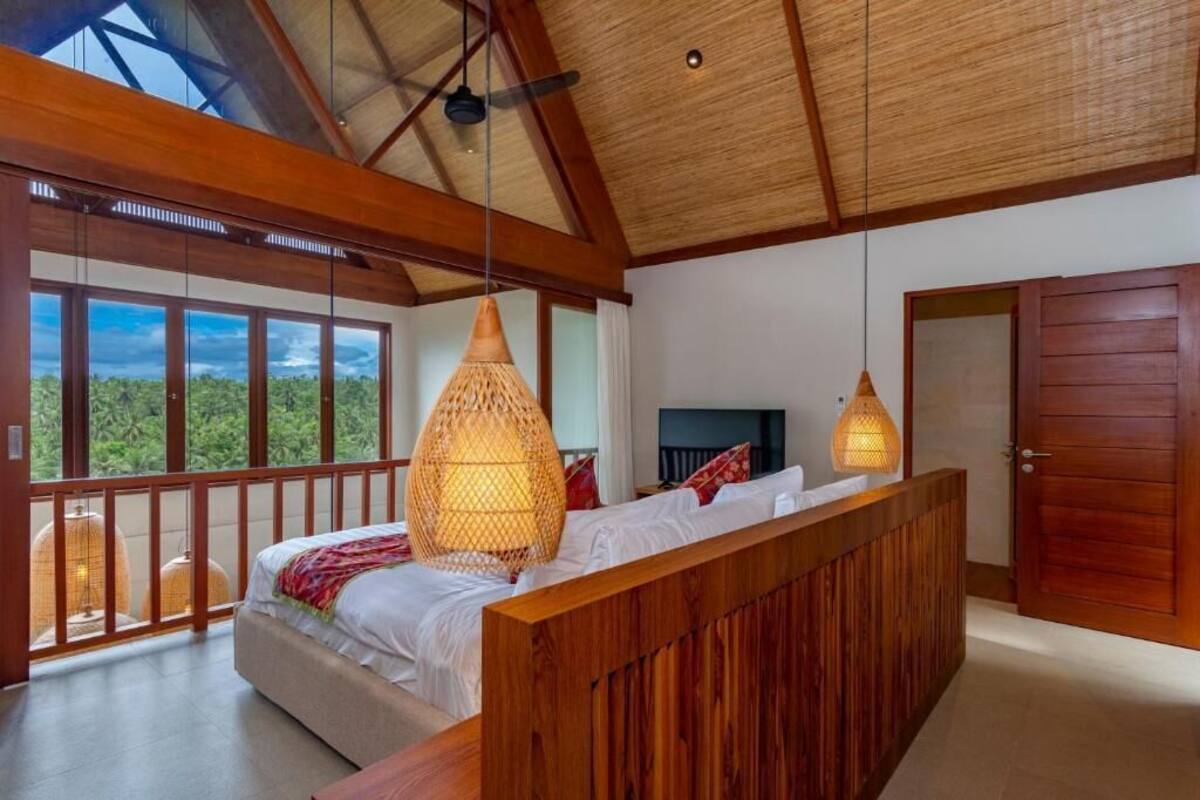 Un dormitorio con una cama grande, cabecera de madera y un balcón con vistas a zonas verdes.
