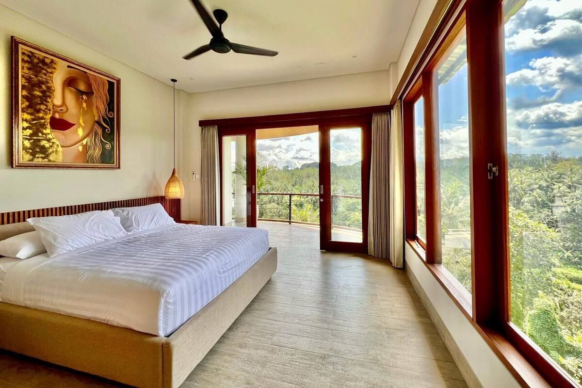 Un dormitorio con una cama grande, un ventilador de techo y vistas a un paisaje montañoso a través de amplios ventanales.