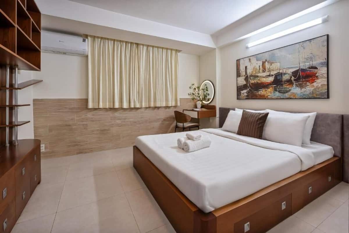 Een moderne hotelkamer met een groot bed, een houten dressoir, een bureau met stoel, een groot schilderij aan de muur en een raam met gordijnen.