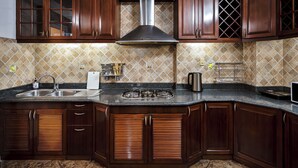 A kitchen with dark wooden cabinets, a stainless steel range hood, a granite countertop, and a tiled backsplash. - Otis Apartment - 457 Rooftop Garden (Ho Chi Minh City)
