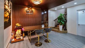 A reception area with a wooden wall, a reception desk, two bar stools, a staircase, and a potted plant. - Otis Apartment - 457 Rooftop Garden (Ho Chi Minh City)