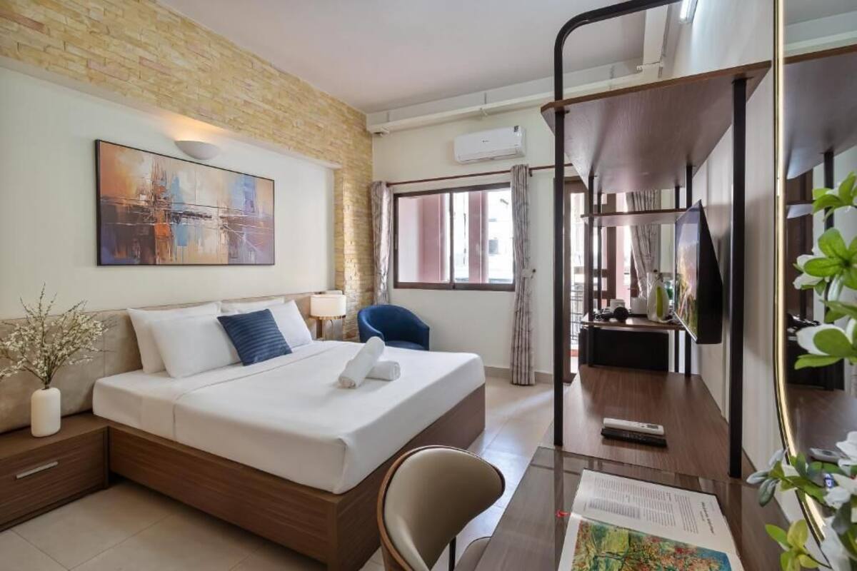 Hotelkamer met een bed, nachtkastje, stoel, bureau en een groot raam.