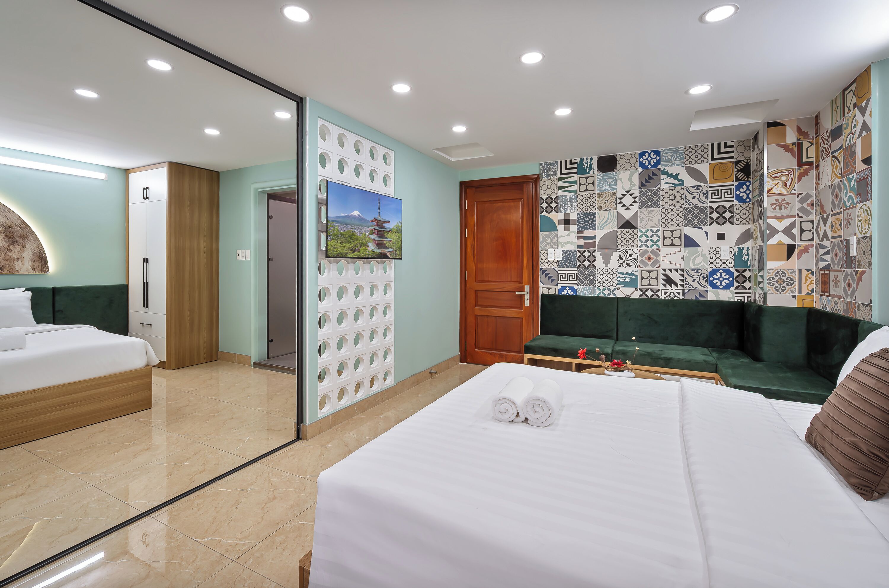Ein Hotelzimmer mit einem Bett, einem grünen Sofa, einem Fernseher und einer Wand mit gemusterten Fliesen.