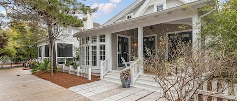 A two-story house with a covered porch, a wooden deck, and a landscaped garden.